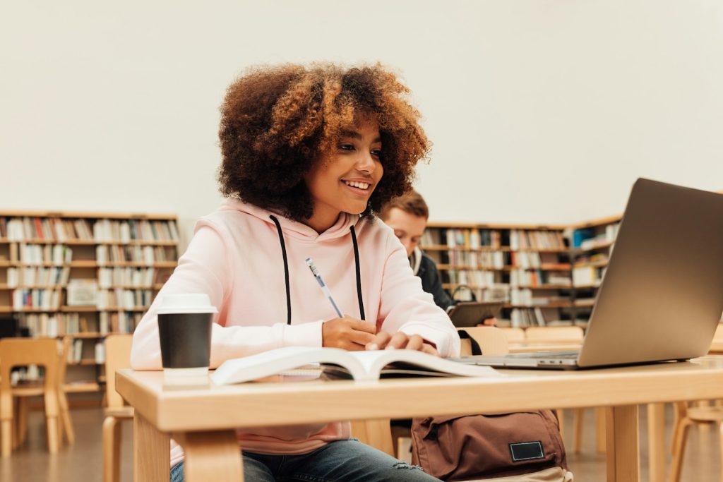 Beautiful smiling girl looking at laptop in library preparing exams