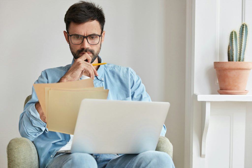 Serious concentrated businessman in spectacles for vision protection, works on laptop computer, stud