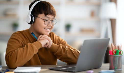 Cheerful asian boy schooler having online lesson from home
